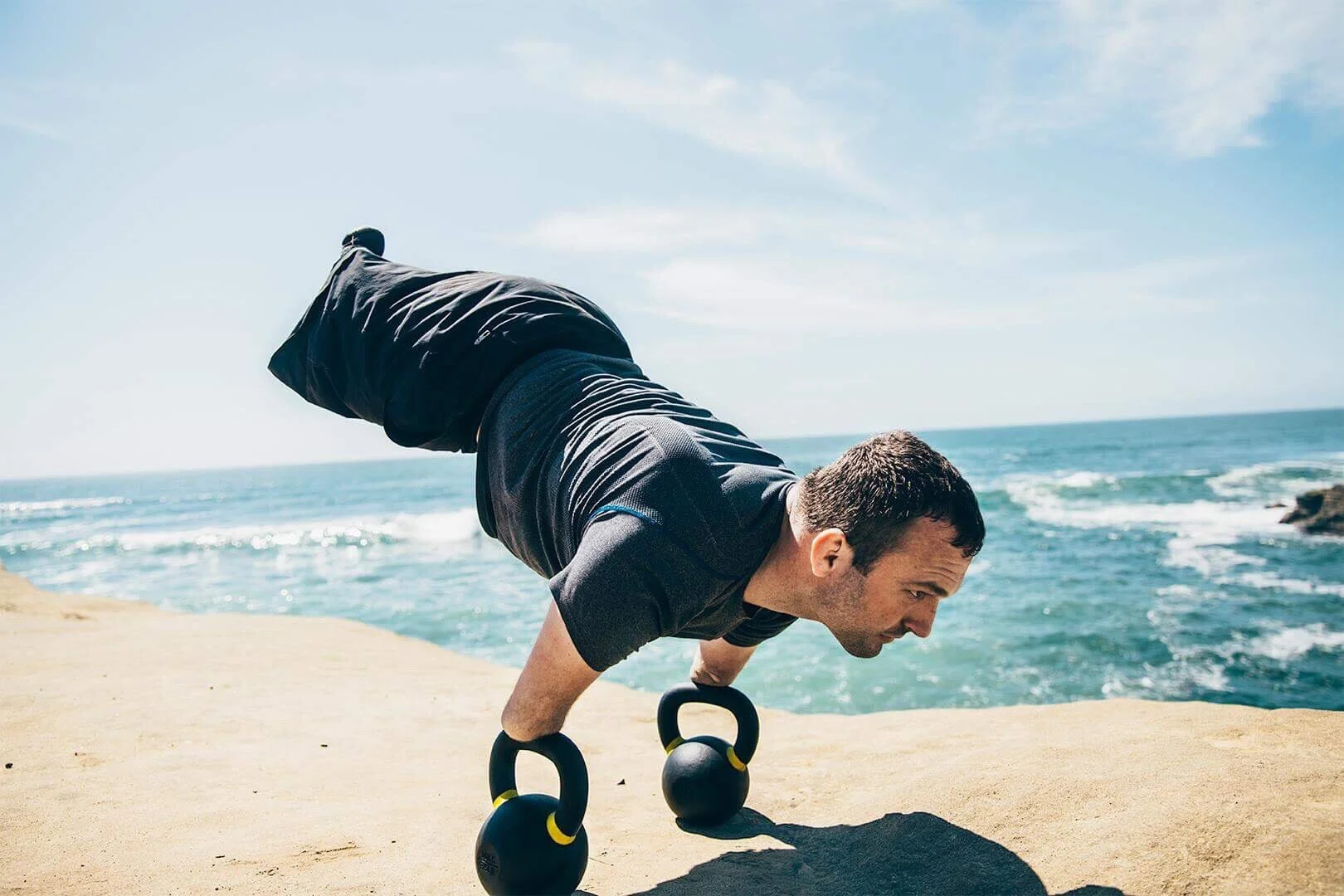 Kyle Maynard holding a plank on kettlebells at the edge of the ocean
