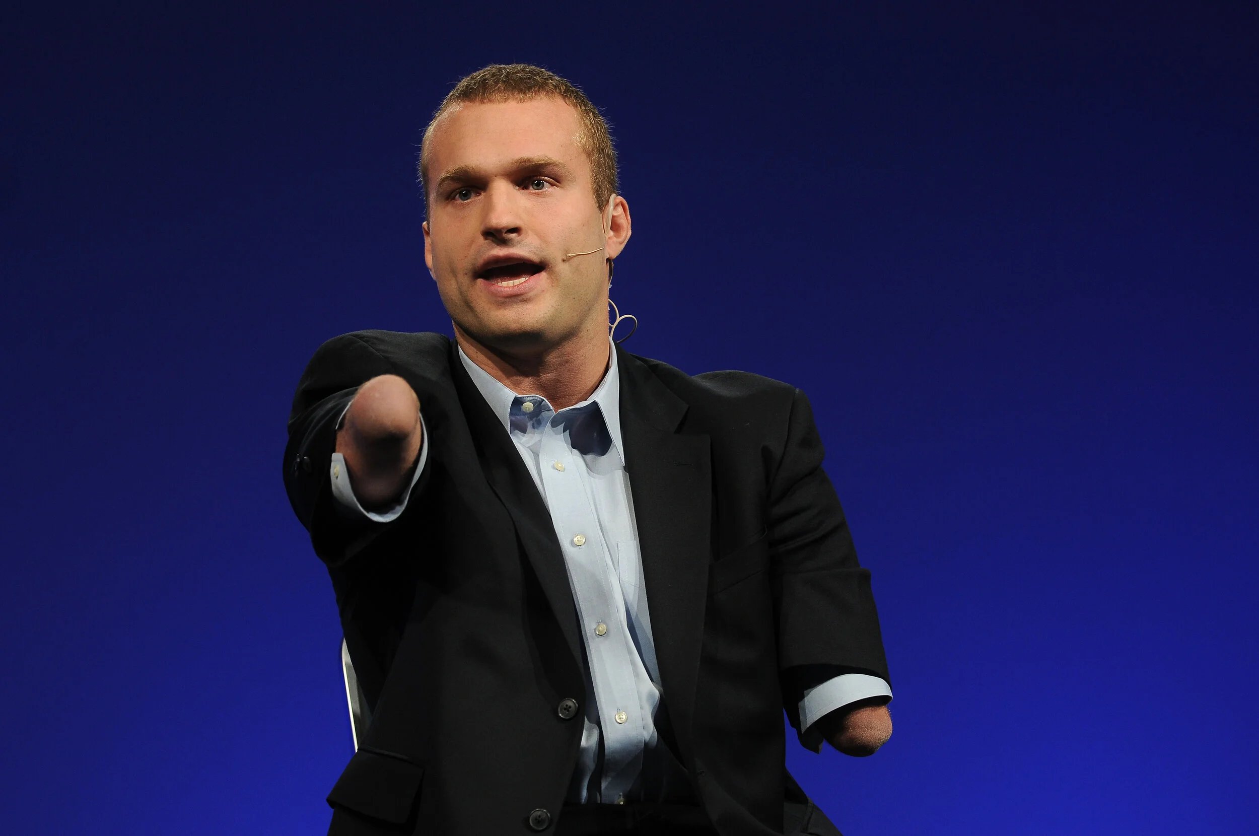 Kyle Maynard speaking on stage in a suit, pointing at the audience