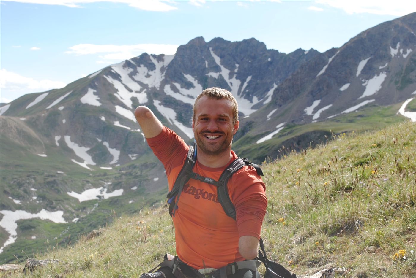 Kyle Maynard smiling on a high mountain ridge with snowy peaks behind him